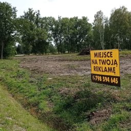 ADAM MIKULSKI - Żółty baner z napisem 'Miejsce na Twoją Reklamę' i numerem telefonu na przygotowanym pod budowę terenie, widok z boku drogi.