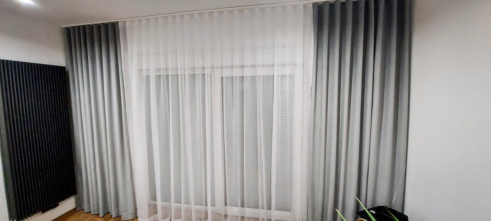 Okno z szarymi i białymi zasłonami, widoczne fałdy materiału i subtelne światło dzienne.