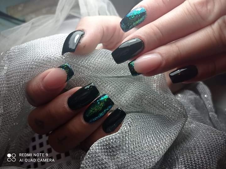 Dłonie prezentują zestawienie czarnych paznokci żelowych z akcentami holograficznego pyłku, na tle srebrzystej tkaniny.