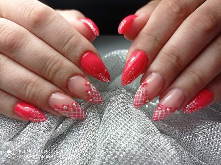 Dłonie z pomalowanymi paznokciami w odcieniach czerwieni i beżu, zdobione siateczką i drobnymi kwiatkami, na srebrnym, połyskującym tle.