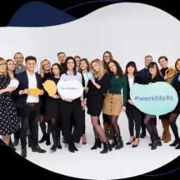 Grupowe zdjęcie zespołu z kolorowymi rekwizytami w kształcie chmurek, na jednej z nich logo Talent Place, na innej napis #worklifefit