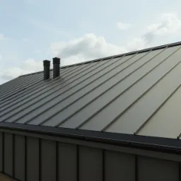 Szary dach z blachy na rąbek stojący z dwoma kominami wentylacyjnymi, widok z dołu na tle błękitnego nieba z chmurami.