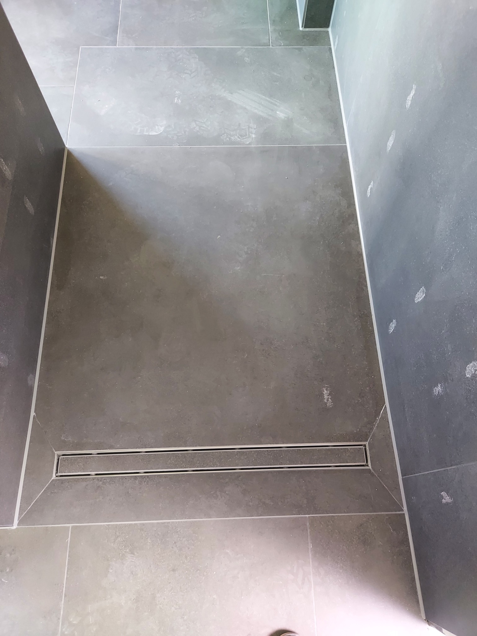 Szare płytki podłogowe z odpływem liniowym w kabinie prysznicowej w Nowogrodźcu. Na ścianach widoczne ślady po pracach wykończeniowych.