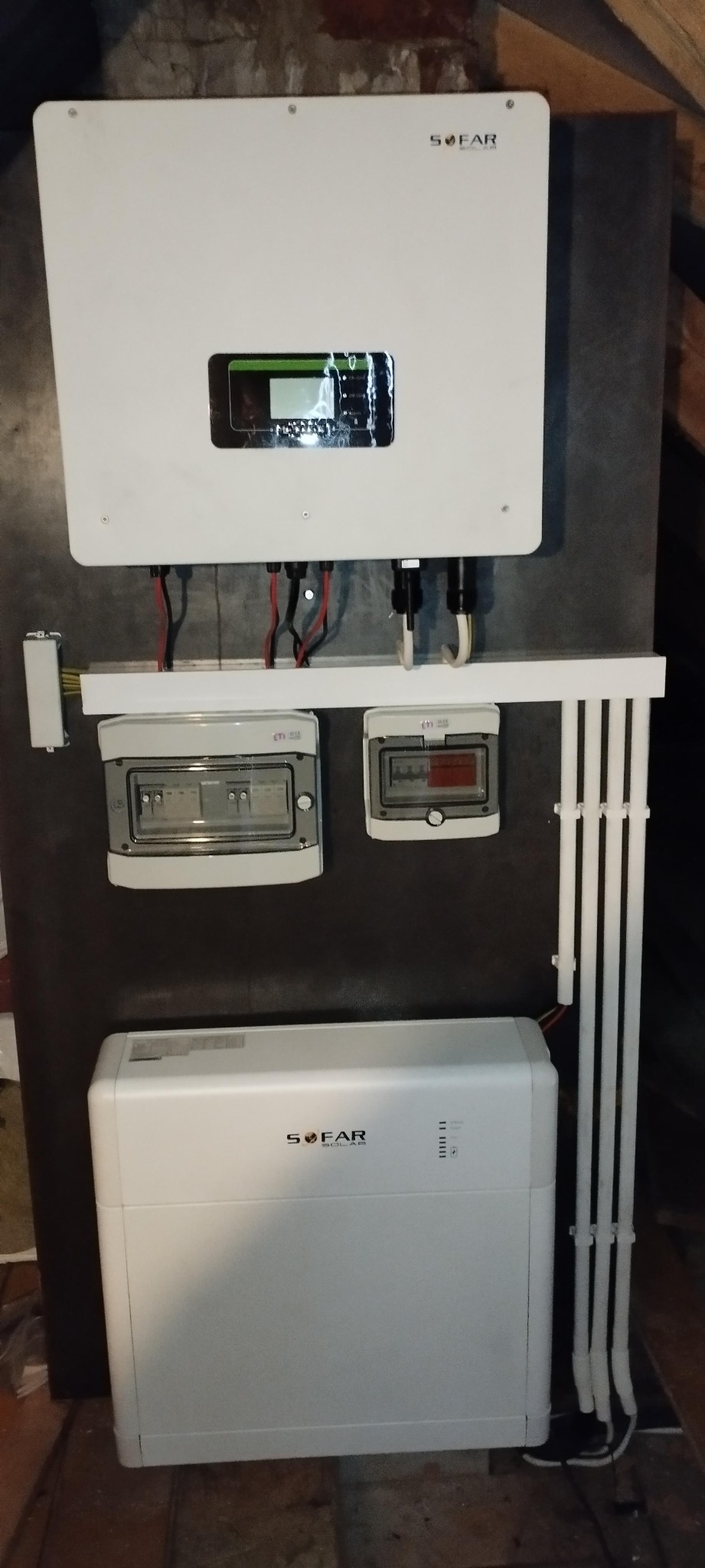 Zamontowany zestaw urządzeń do instalacji fotowoltaicznej marki Sofar Solar, z widocznymi zabezpieczeniami i przewodami, umieszczony na ciemnej ścianie w pomieszczeniu.