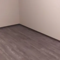 Ukończone układanie paneli podłogowych w rogu pokoju, widoczna ściana pomalowana na jasny kolor.