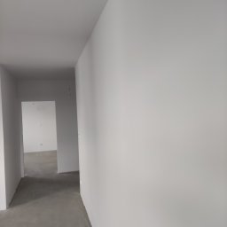 Molart - Wnętrze po malowaniu: białe ściany, szara podłoga i otwarte przejścia. Widok z perspektywy, ukazujący świeżo odnowione pomieszczenie.