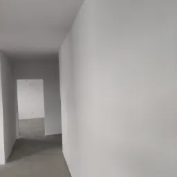 Wnętrze po malowaniu: białe ściany, szara podłoga i otwarte przejścia. Widok z perspektywy, ukazujący świeżo odnowione pomieszczenie.