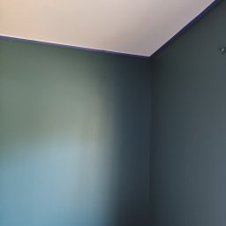 Molart - Pomieszczenie po malowaniu na szaro, z widocznym odcięciem od sufitu zabezpieczonym taśmą malarską. Świeżo odmalowane ściany, narożnik pokoju.