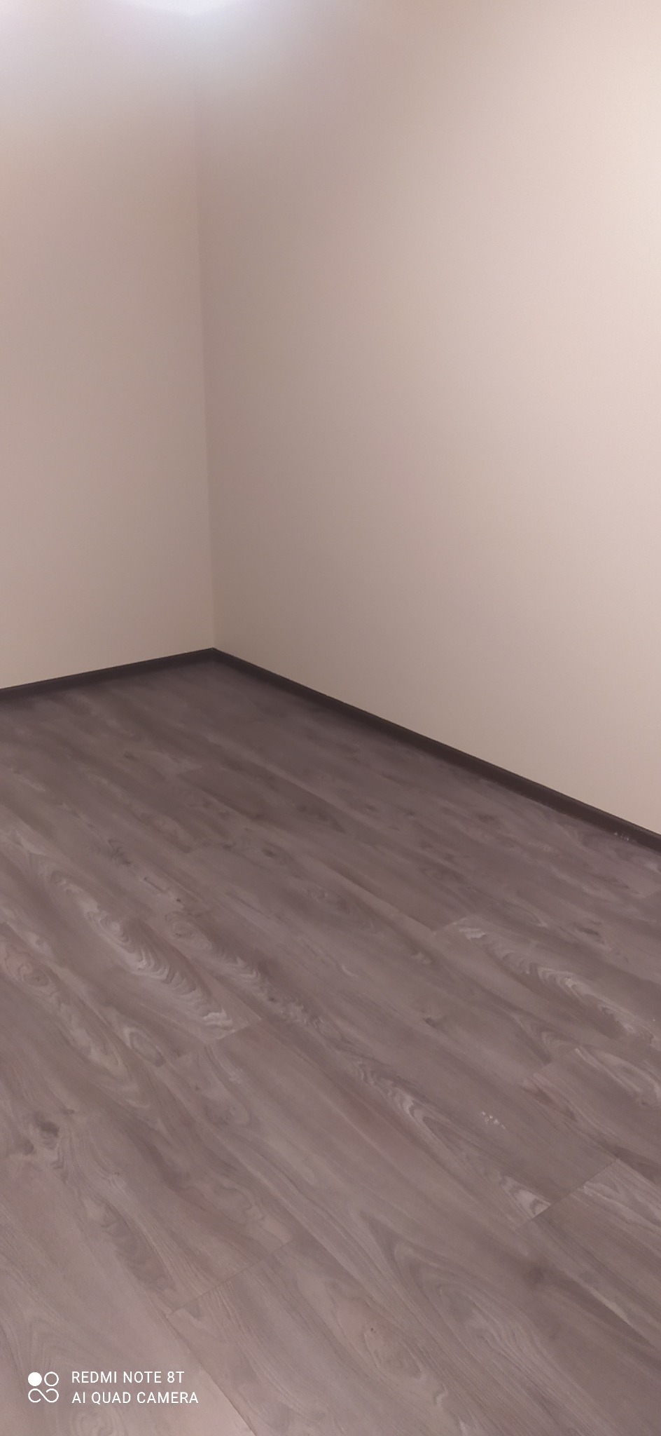 Ukończone układanie paneli podłogowych w rogu pokoju, widoczna ściana pomalowana na jasny kolor.