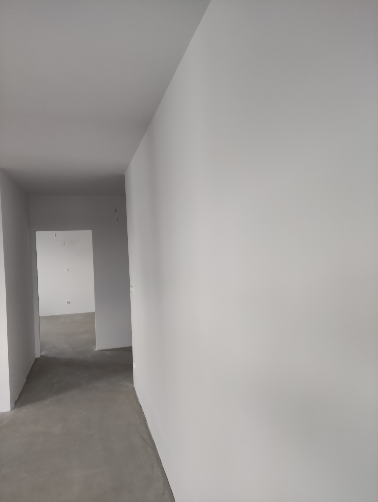 Wnętrze po malowaniu: białe ściany, szara podłoga i otwarte przejścia. Widok z perspektywy, ukazujący świeżo odnowione pomieszczenie.
