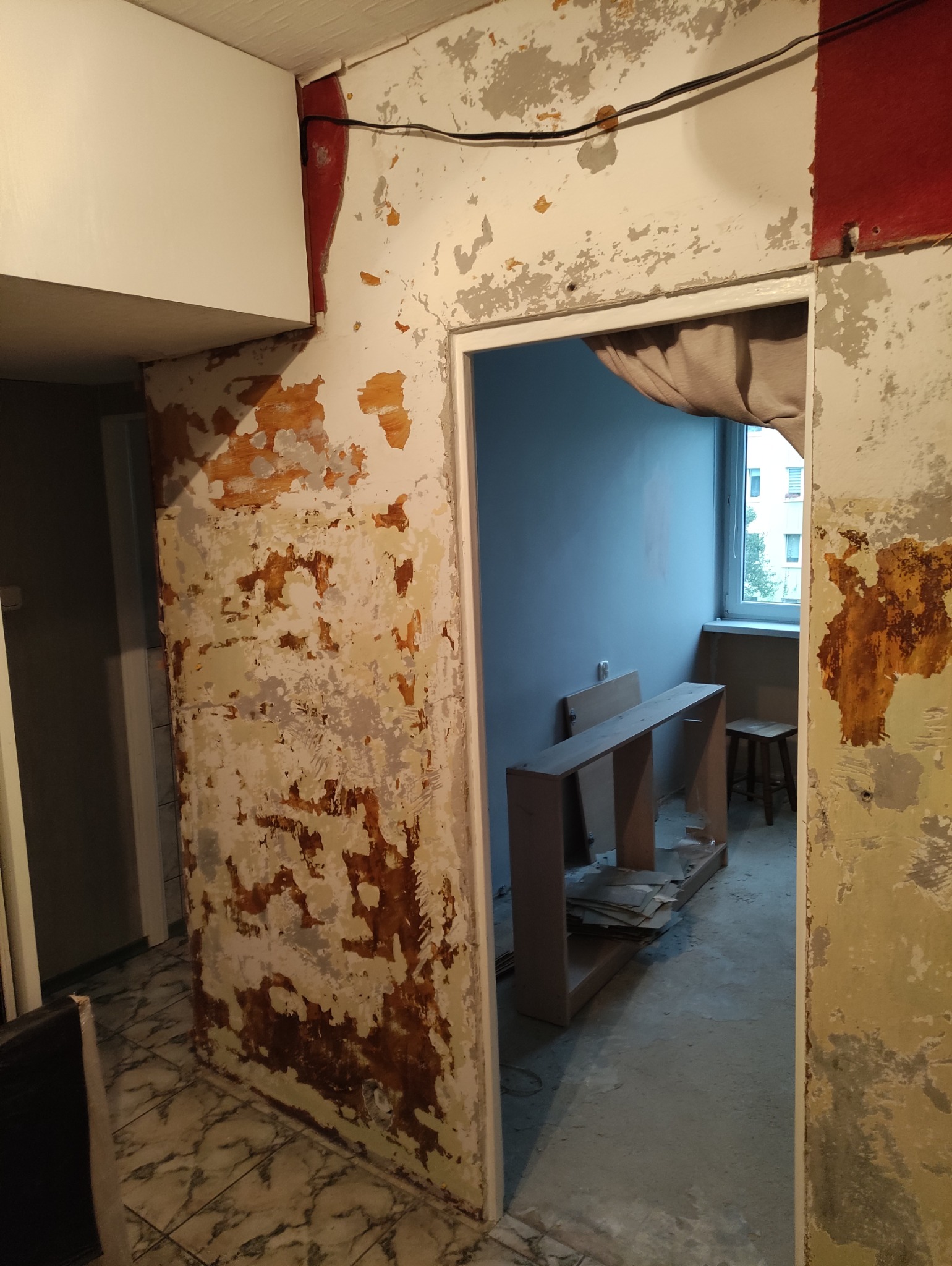 Wnętrze w trakcie remontu: ściany ze śladami starej farby, odsłonięte fragmenty podłoża, widoczne przygotowania do dalszych prac wykończeniowych.