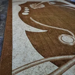 Brązowy dywan z kremowymi wzorami w kształcie liści i abstrakcyjnych linii, widoczny z bliska pod kątem.