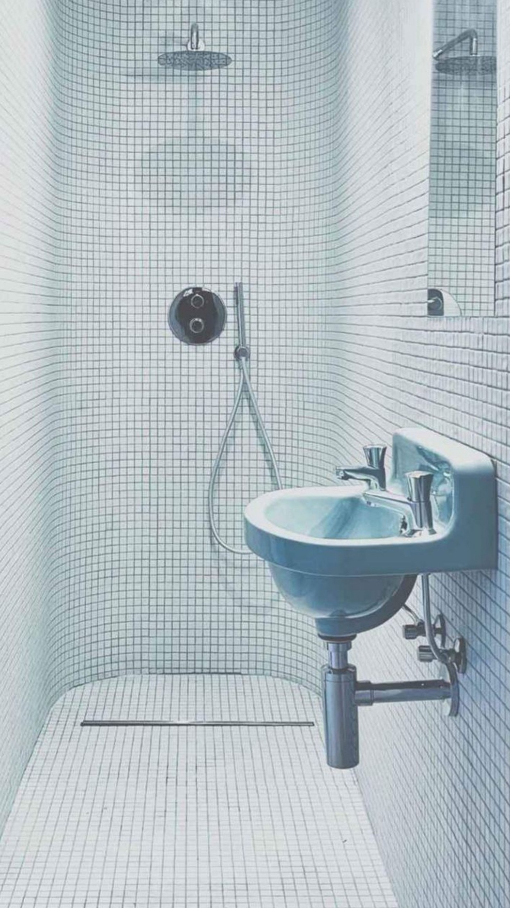 Niebieska umywalka zamontowana na ścianie wyłożonej białą mozaiką w minimalistycznej kabinie prysznicowej z odpływem liniowym.