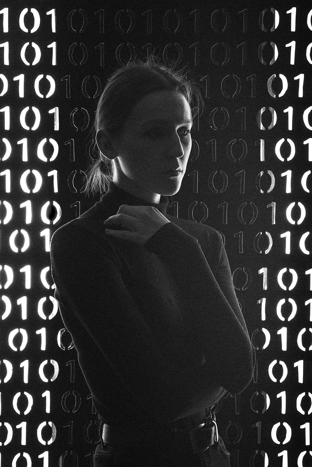 Portret kobiety w półcieniu na tle ściany z podświetlonymi binarnymi kodami zero-jedynkowymi, artystyczne ujęcie.