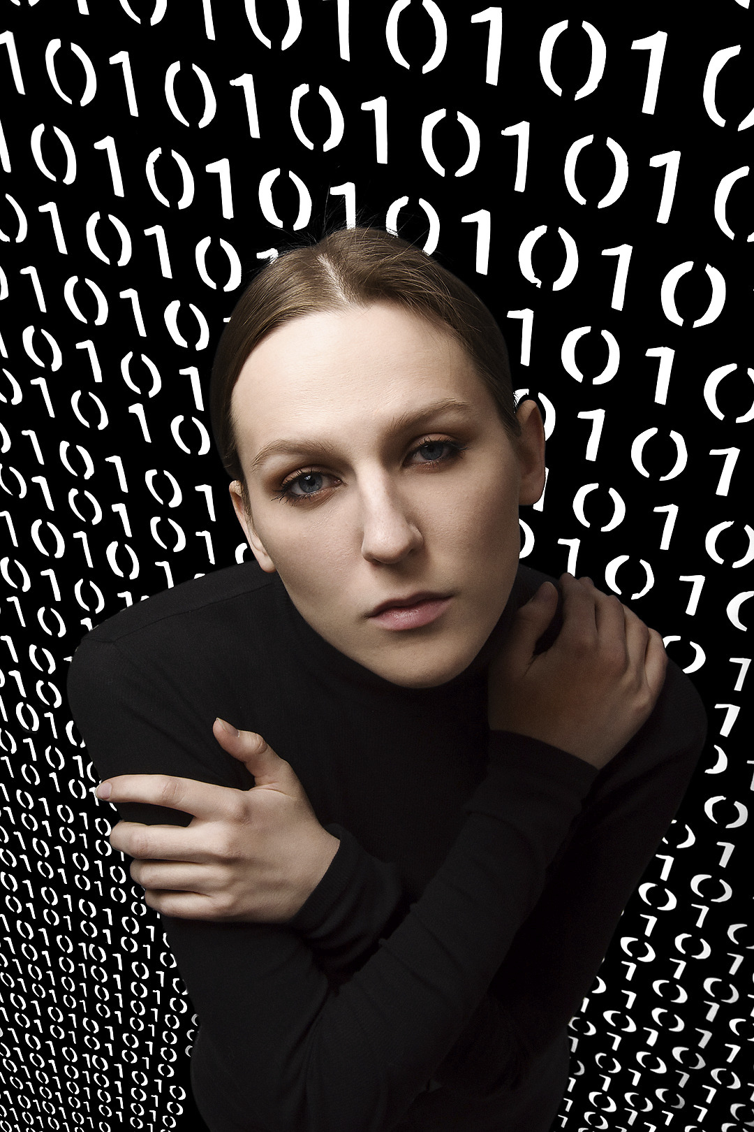 Portret kobiety w czarnym golfie na tle cyfrowego wzoru zero-jedynkowego, ujęcie z dołu podkreślające spojrzenie.