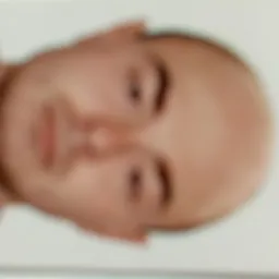 Rozmazane zdjęcie twarzy mężczyzny z krótkimi włosami, skierowanej w lewą stronę, na jasnym tle.