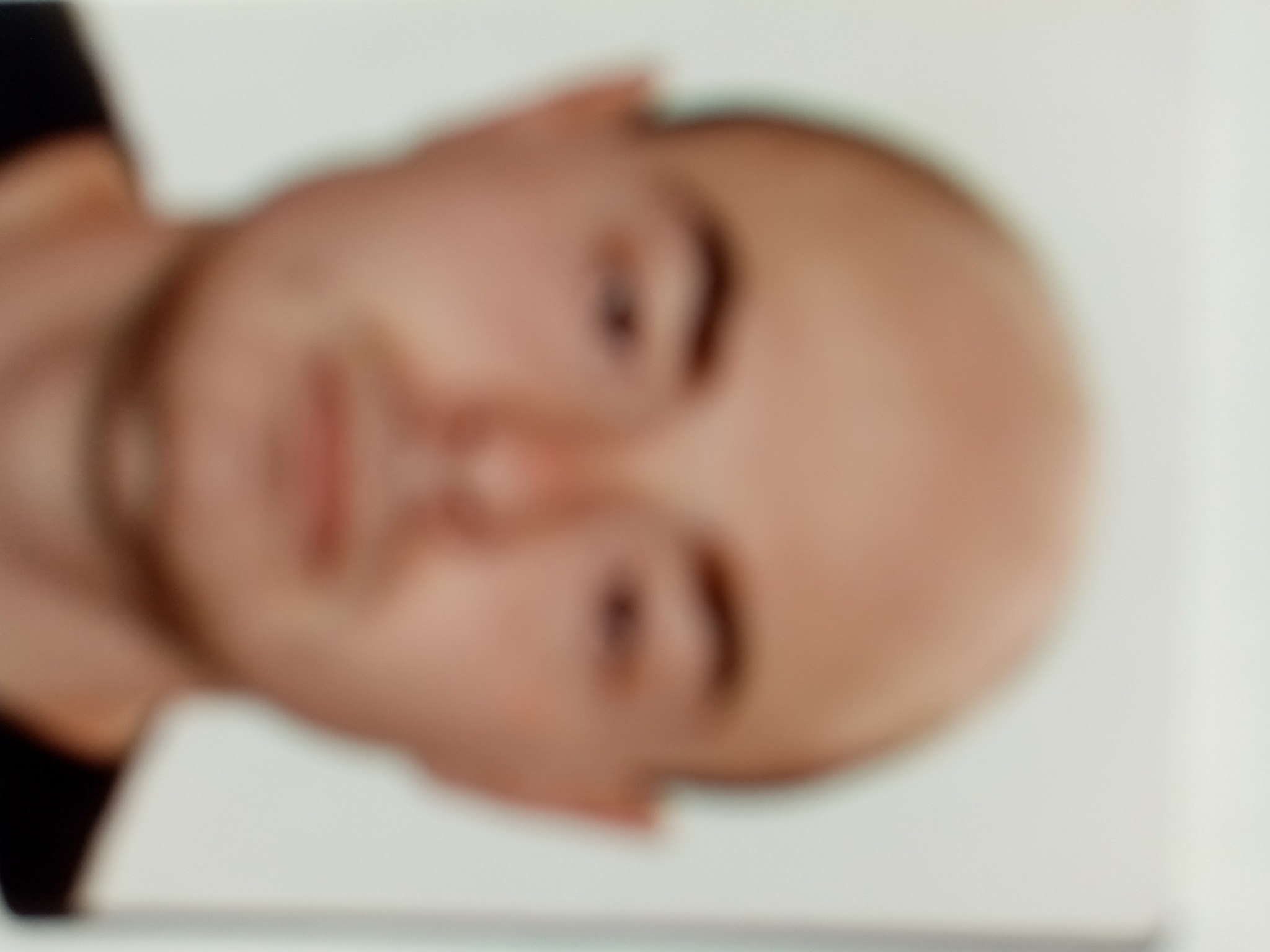 Rozmazane zdjęcie twarzy mężczyzny z krótkimi włosami, skierowanej w lewą stronę, na jasnym tle.