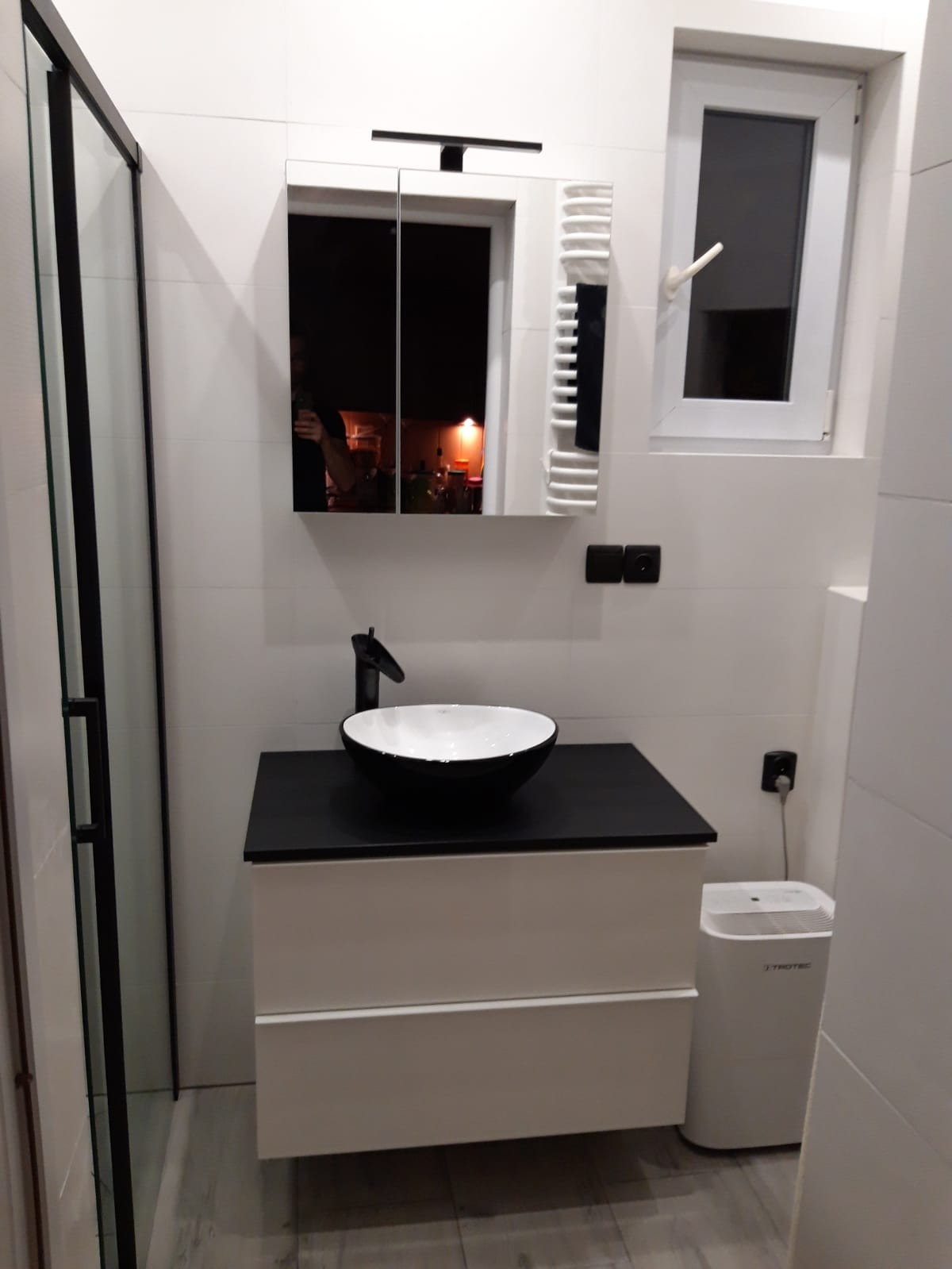 Nowoczesna łazienka z białą armaturą, czarnym blatem i okrągłą umywalką, widoczny grzejnik drabinkowy i osuszacz powietrza Trotec.