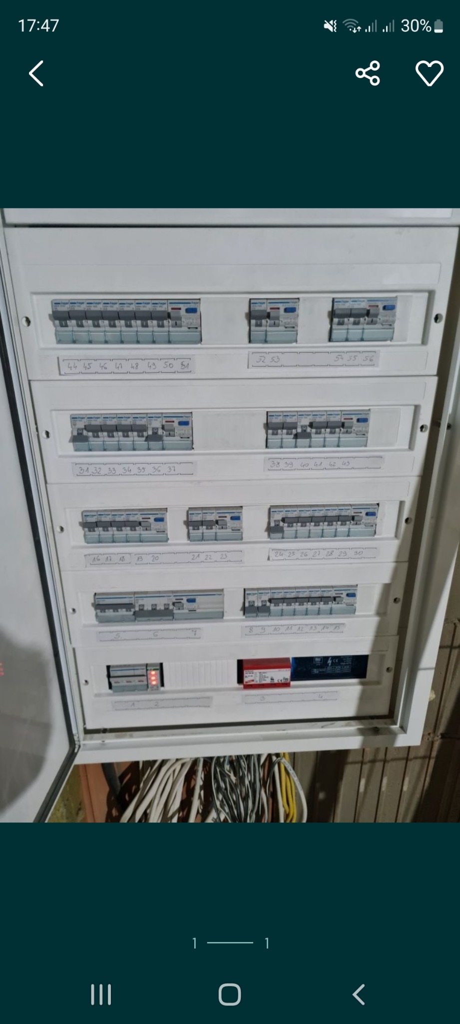 Otwarta skrzynka rozdzielcza z bezpiecznikami, opisana numerami, widoczne przewody w dolnej części.