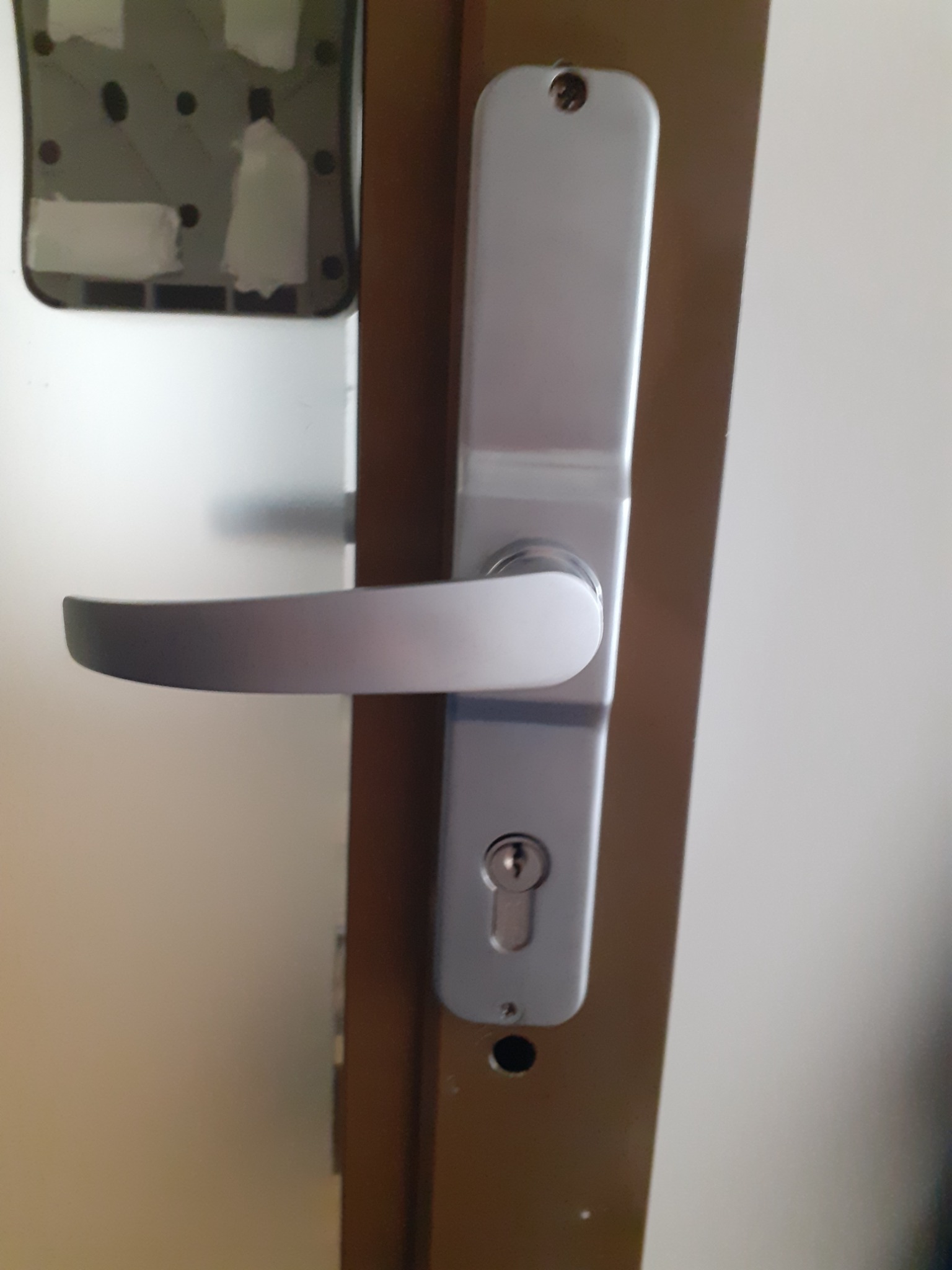 Zamknięcie drzwi z srebrną klamką i wkładką zamka, widoczne ślady po taśmie malarskiej na ościeżnicy.