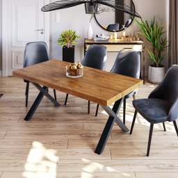 ARECO Spółka z o.o. - Rustykalny stół z drewnianym blatem i czarnymi, metalowymi nogami w kształcie litery X, otoczony czterema szarymi krzesłami w nowoczesnym wnętrzu z drewnianą podłogą i dekoracjami.