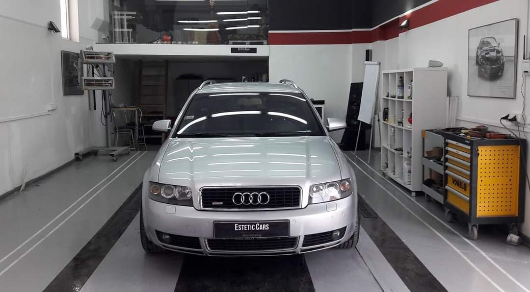 Srebrne Audi kombi w warsztacie, widok z przodu, z widocznym logo 'Estetic Cars' na tablicy rejestracyjnej, na podłodze białe pasy, w tle regał z narzędziami i drabina.