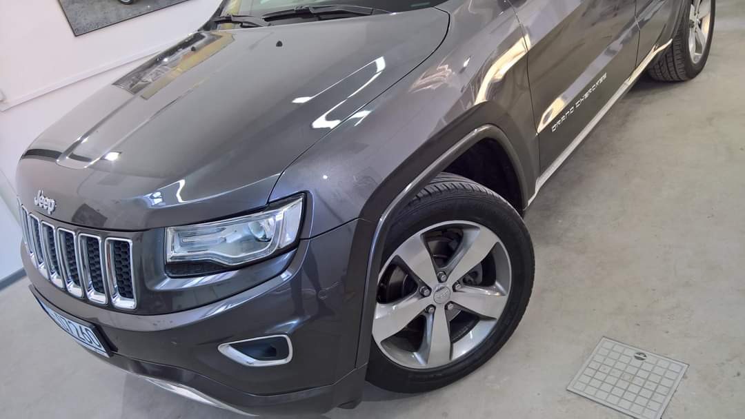 Błyszczący, szary Jeep Grand Cherokee po zabiegach pielęgnacyjnych, widoczny z przodu i boku, z wyraźnie odbijającym światło lakierem.