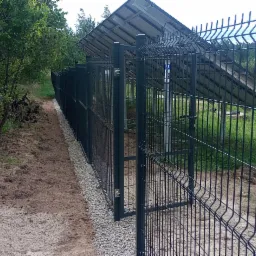 Nowoczesne, grafitowe ogrodzenie panelowe z podmurówką z drobnego kamienia, widok od strony posesji z widocznymi panelami fotowoltaicznymi w tle.