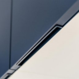 ASPEKT meble - Detal minimalistycznej szafki z ciemnoniebieskimi frontami i subtelnymi, wpuszczanymi uchwytami, sfotografowanej pod kątem.