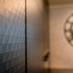 ASPEKT meble - Ciemna szafa wnękowa z geometrycznym wzorem trójkątów, widoczny zegar dekoracyjny w tle i logo firmy Aspekt Meble