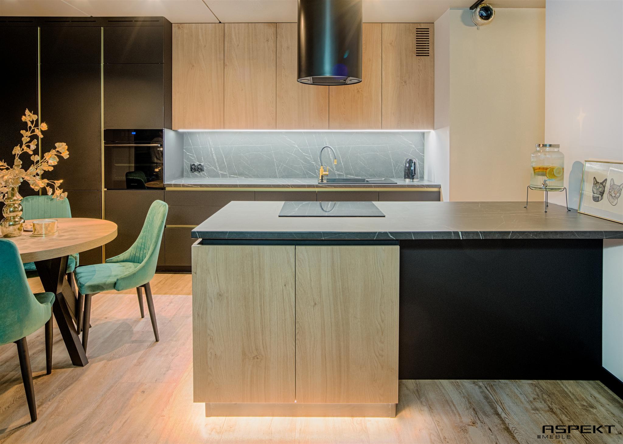 Nowoczesna kuchnia z czarnymi i drewnianymi szafkami, marmurowym blatem, okrągłym stołem z turkusowymi krzesłami i oświetleniem LED pod szafkami i wyspą.