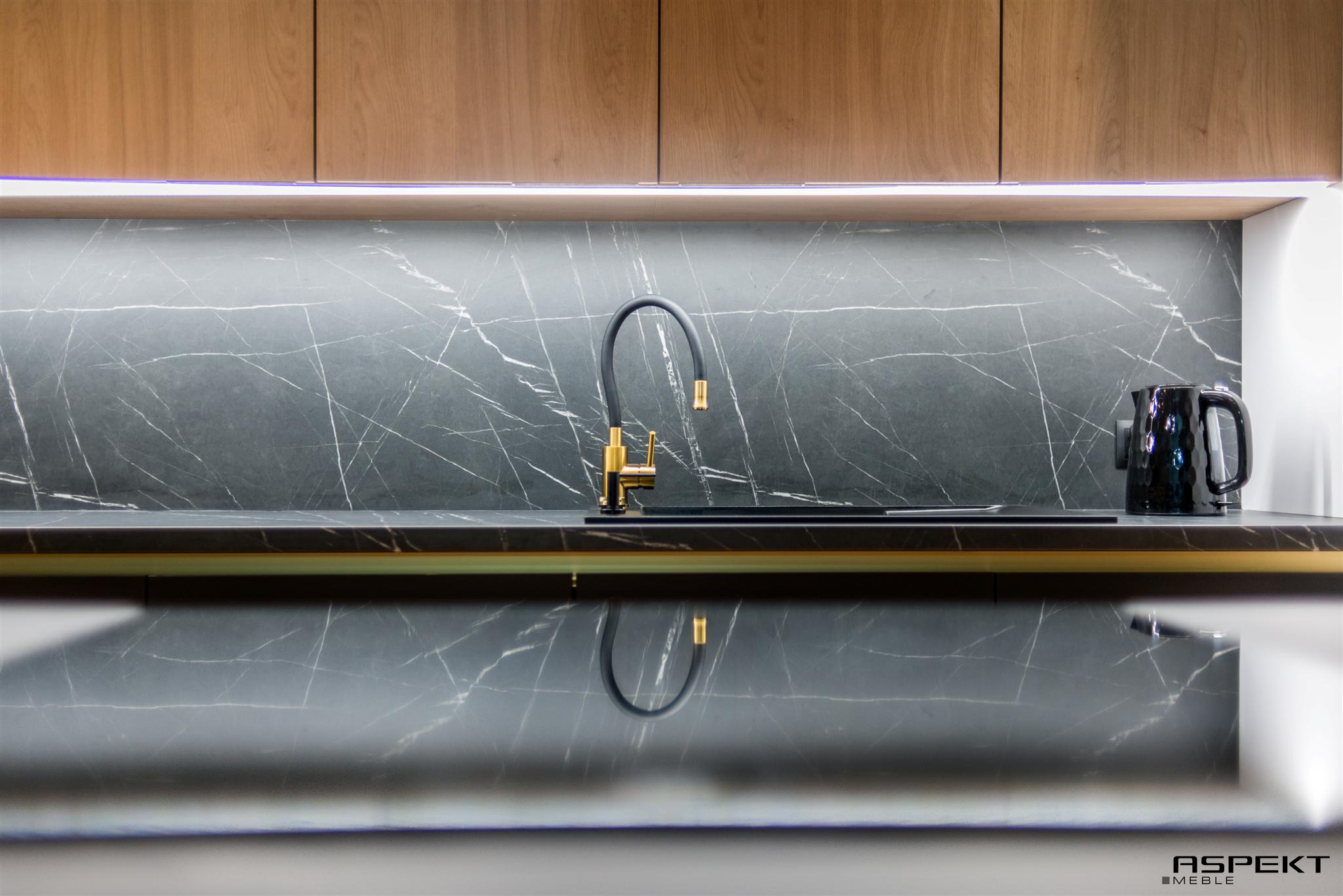 Nowoczesna kuchnia: czarny marmurkowy blat i backsplash, złota bateria z czarną wylewką, drewniane szafki górne podświetlone listwą LED, czarny czajnik elektryczny.