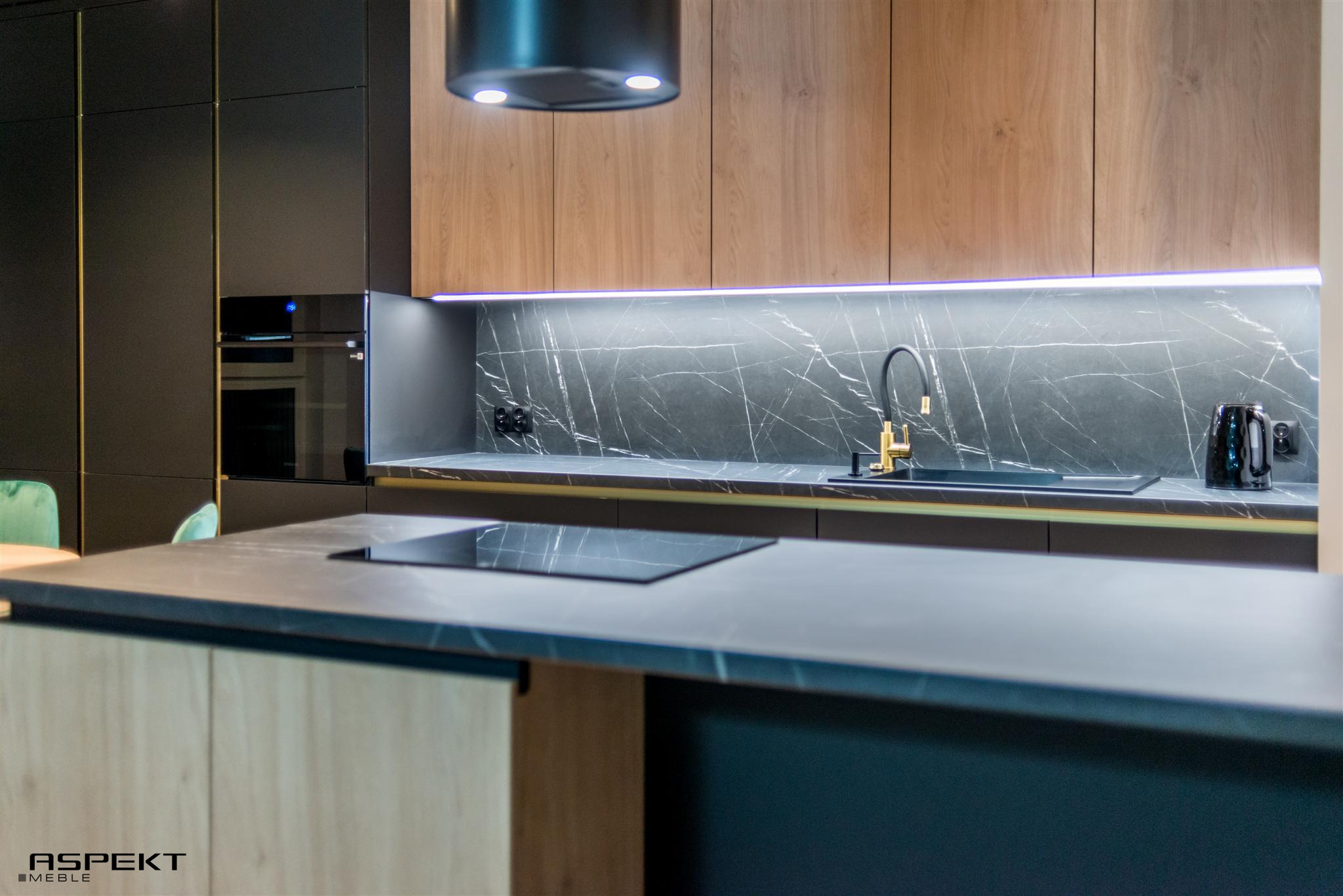 Nowoczesna kuchnia z czarnymi frontami szafek, drewnianymi akcentami, marmurowym blatem i złotą armaturą, oświetleniem LED podszafkowym i wyspą z płytą indukcyjną.