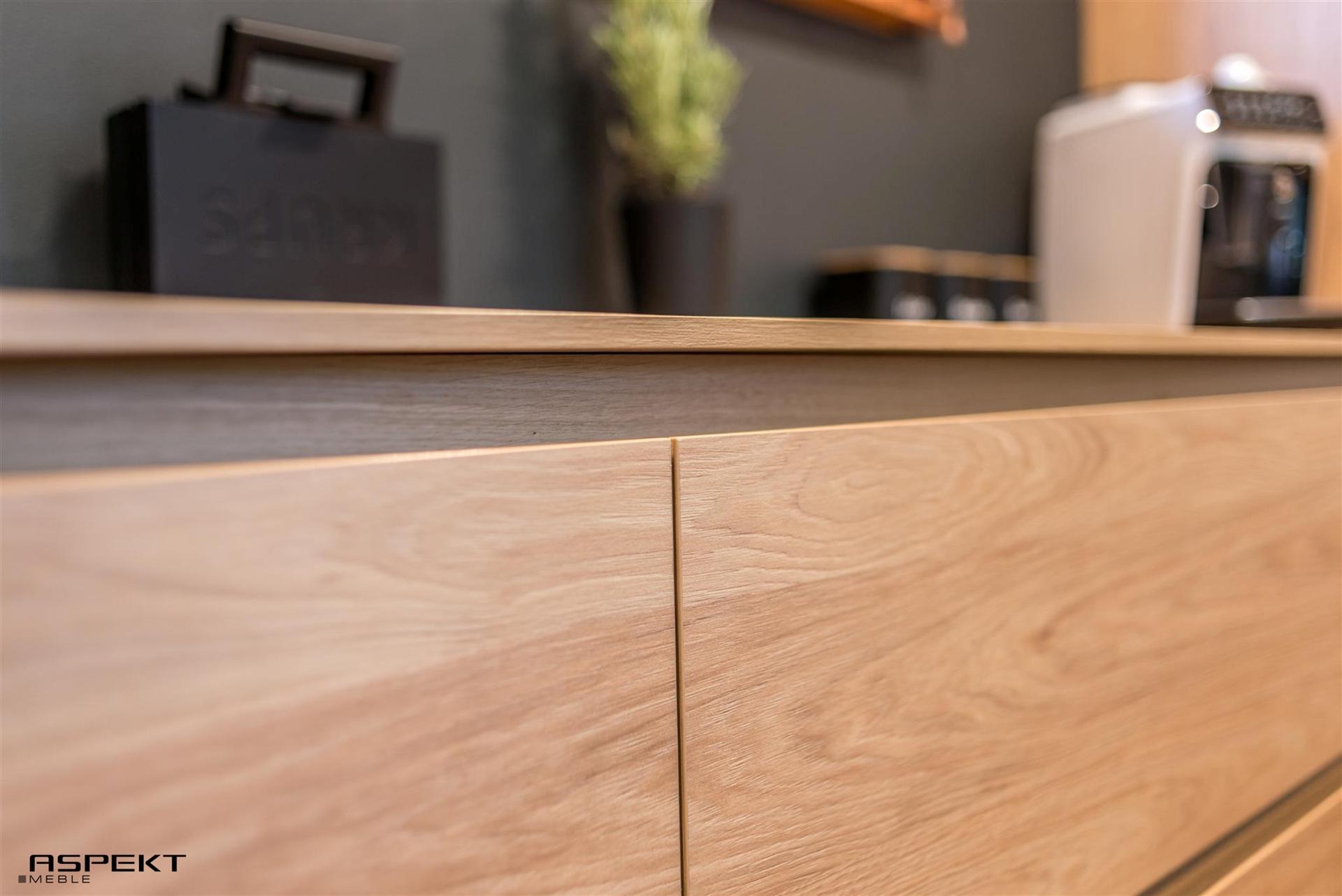 Fragment szafki kuchennej z jasnego drewna, widoczne detale usłojenia, na blacie akcesoria kuchenne i dekoracje.