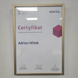 Oprawiony w złotą ramkę certyfikat Klubu Liderów Warty dla Adriana Witka, wiszący na jasnej ścianie.