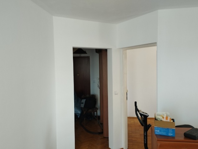 Świeżo pomalowane na biało ściany mieszkania z widocznymi dwoma otwartymi przejściami do innych pomieszczeń, w jednym z nich widoczny odkurzacz.