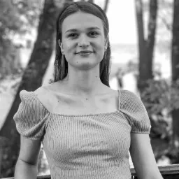 Portret uśmiechniętej młodej kobiety w prążkowanym topie z bufkami na tle drzew w czerni i bieli.