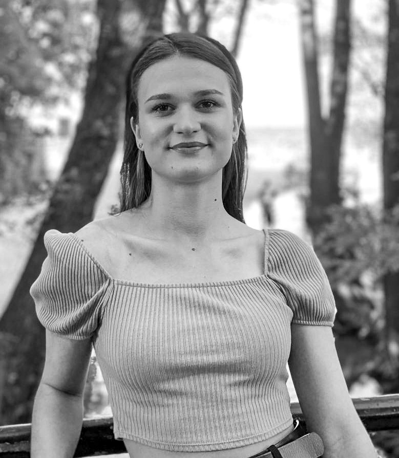 Portret uśmiechniętej młodej kobiety w prążkowanym topie z bufkami na tle drzew w czerni i bieli.