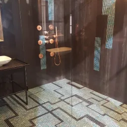 Nowoczesna kabina prysznicowa z mozaiką w geometryczny wzór na podłodze i ścianach, armatura w kolorze miedzianym, zrealizowana w Krakowie.