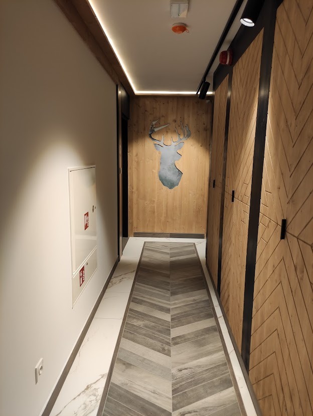 Korytarz z drewnianą boazerią w jodełkę, szarą podłogą w chevron i dekoracją ścienną w kształcie głowy jelenia.