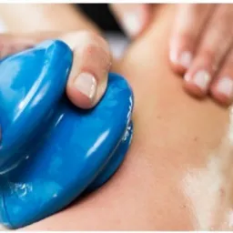 Dłonie terapeuty wykonują zabieg bańkami chińskimi na natłuszczonej skórze pacjenta, widoczne zaczerwienienia.