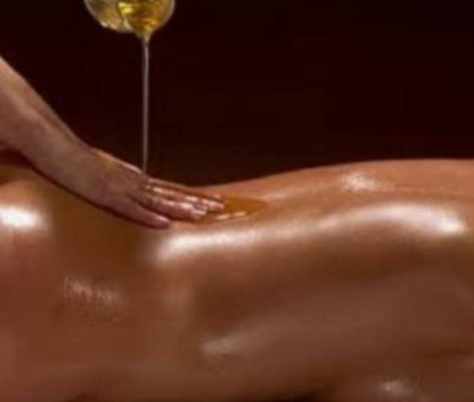 Olej spływa na plecy podczas zabiegu, dłoń masuje skórę w ciepłym oświetleniu.