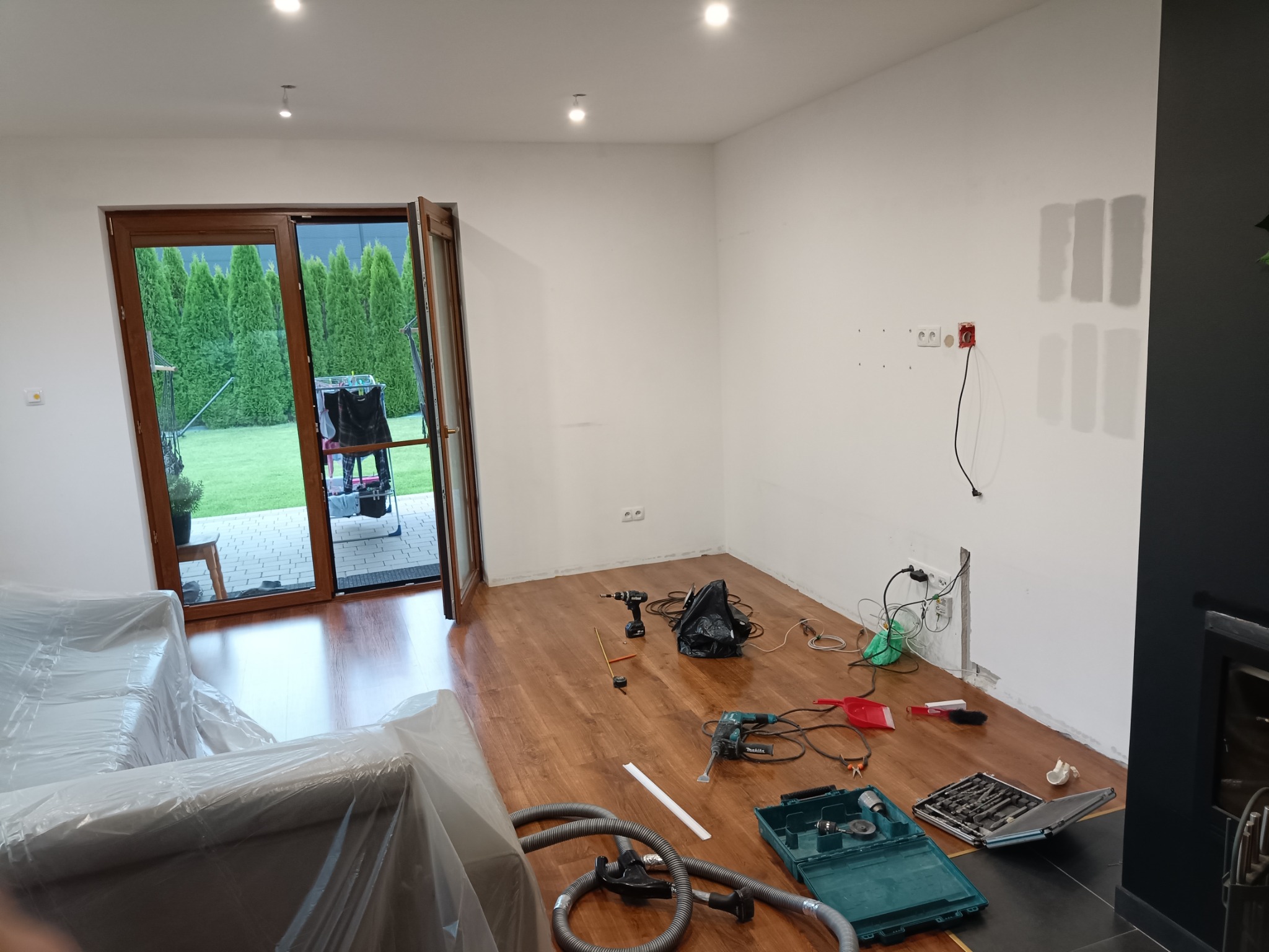 Pokój w trakcie remontu: podłoga z paneli, ściany przygotowane do prac wykończeniowych, widoczne narzędzia i zabezpieczone meble folią.