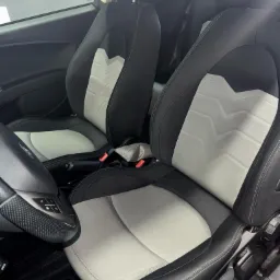 Wnętrze samochodu z czarno-szarymi skórzanymi fotelami sportowymi z charakterystycznym wzorem w jodełkę na oparciach i karbonowym wykończeniem kierownicy.