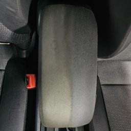 Jednodniowy Garage - Częściowo wyczyszczony, szary podłokietnik samochodowy, widoczna różnica w kolorze i strukturze tkaniny po czyszczeniu, obok czarny fotel z perforowaną tapicerką i czerwony zatrzask pasa...