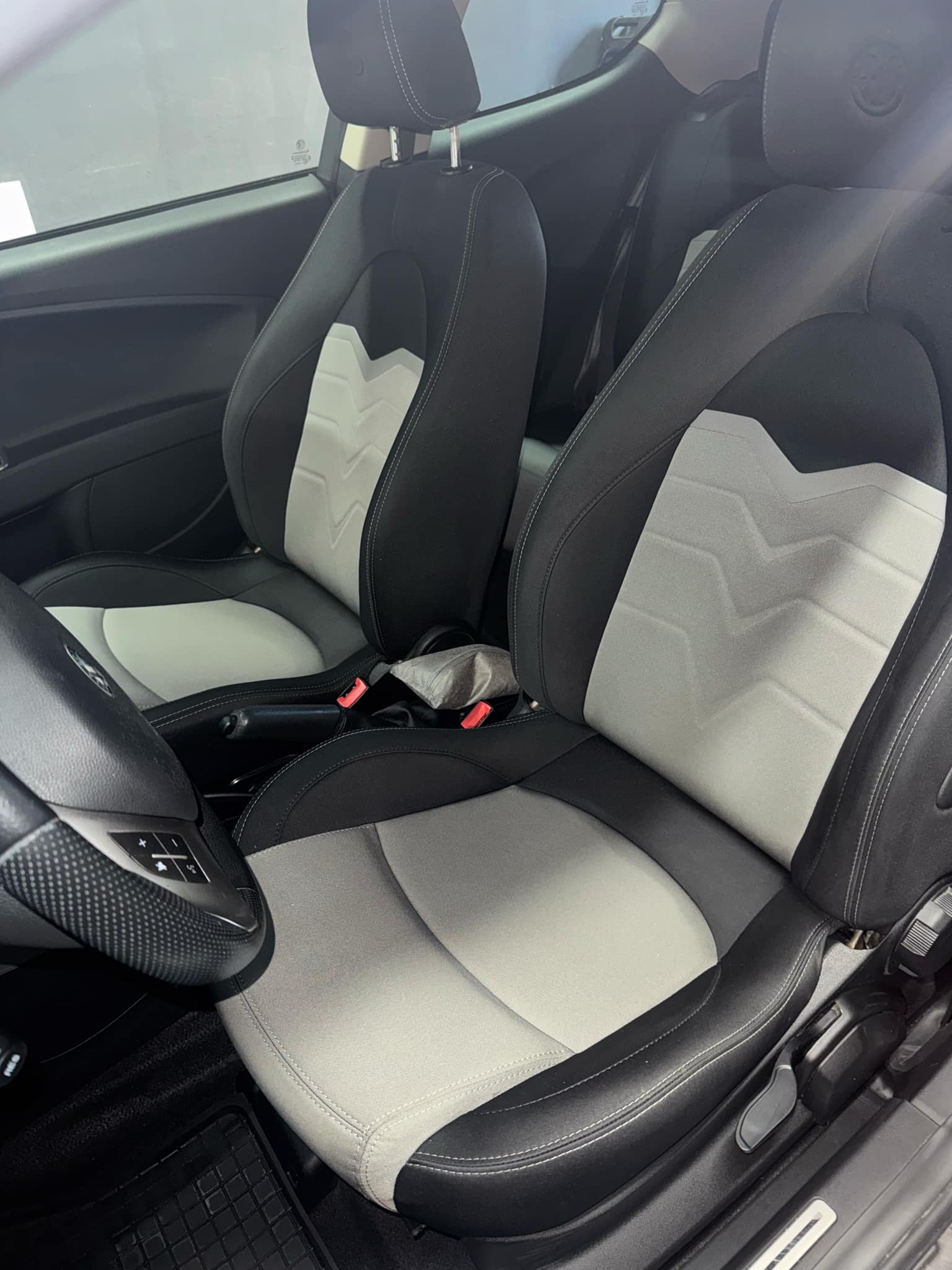 Wnętrze samochodu z czarno-szarymi skórzanymi fotelami sportowymi z charakterystycznym wzorem w jodełkę na oparciach i karbonowym wykończeniem kierownicy.