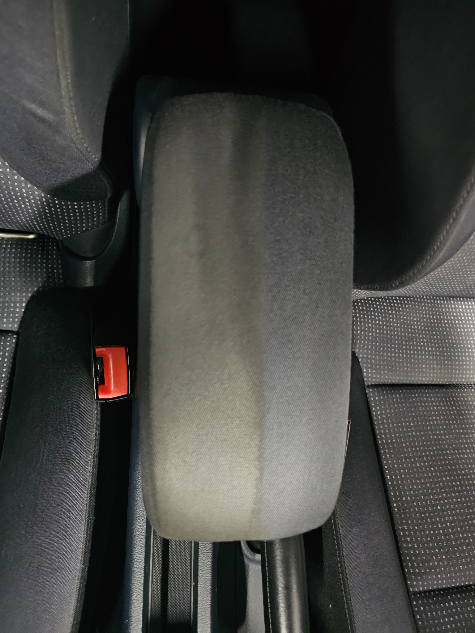 Częściowo wyczyszczony, szary podłokietnik samochodowy, widoczna różnica w kolorze i strukturze tkaniny po czyszczeniu, obok czarny fotel z perforowaną tapicerką i czerwony zatrzask pasa...