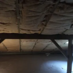 Poddasze z widoczną izolacją z wełny mineralnej między krokwiami, zabezpieczoną sznurkiem, widok z dołu.