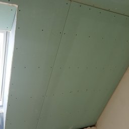 JarBud - Montaż płyt karton gips na poddaszu, widoczne wkręty mocujące, okno dachowe w lewym górnym rogu.