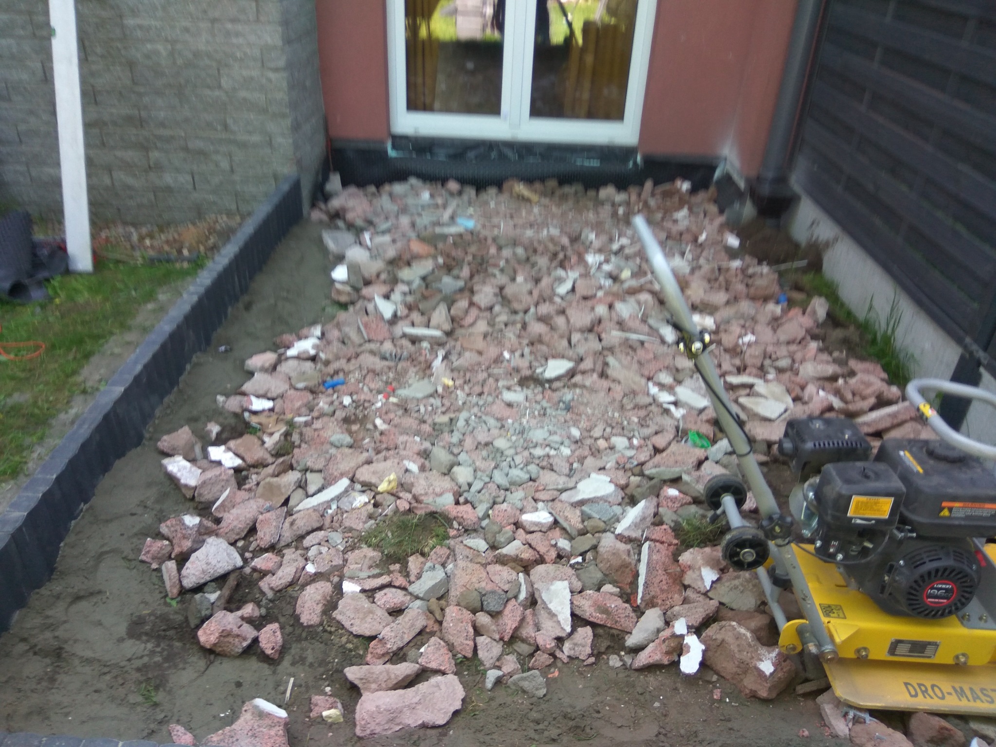 Przygotowanie podłoża pod nawierzchnię: wyrównywanie terenu gruzem i ubijanie zagęszczarką wzdłuż obrzeży posesji.